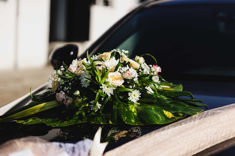 A fresh floral arrangement featuring pale pink and cream roses, white daisies, and small white baby's breath, accented with lush green leaves and foliage, arranged in an elegant bouquet with a glossy 